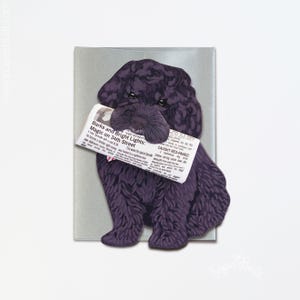 May include: A paper cutout of a black dog holding a newspaper in its mouth. The newspaper has the headline "Barks and Bright Lights: Magic on 34th Street" and the words "Caught Red-Pawed". The dog is on a gray background.