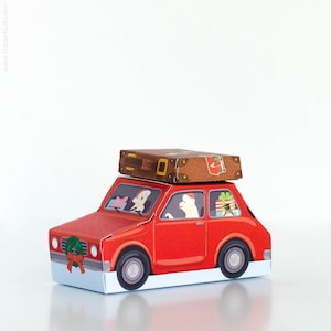 May include: A red paper car with a brown suitcase on top. The car has a Christmas wreath on the front and illustrations of passengers and gifts inside. The car's wheels are black, and the base is white.