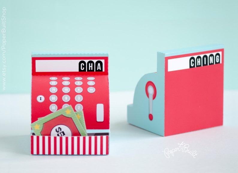 May include: A red and white paper cash register with a blue and white top. The register has a keypad with numbers and a display that says "CHA". There are also two green paper bills with stars and the number "5" on them.