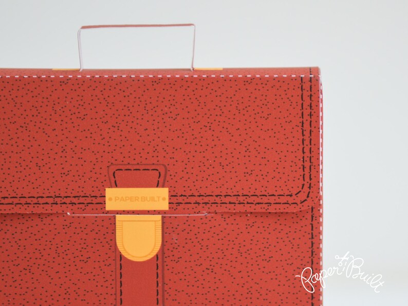 May include: Red leather-look briefcase with a handle and a clasp that says "PAPER BUILT".