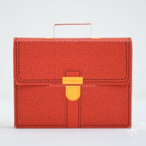 May include: A red leather-textured briefcase with a yellow clasp and a black handle. The briefcase has a stitched design around the edges.