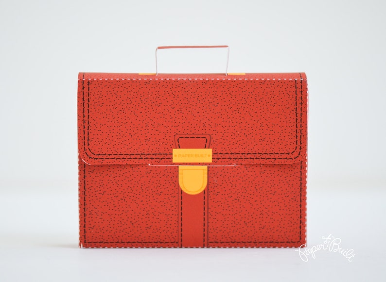 May include: A red leather-textured briefcase with a yellow clasp and a black handle. The briefcase has a stitched design around the edges.