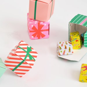 May include: A collection of colorful origami gift boxes with various patterns, including red and white stripes, pink with red stars, green with white stripes, and yellow with a birthday cake design. Some boxes are open, revealing smaller boxes inside.