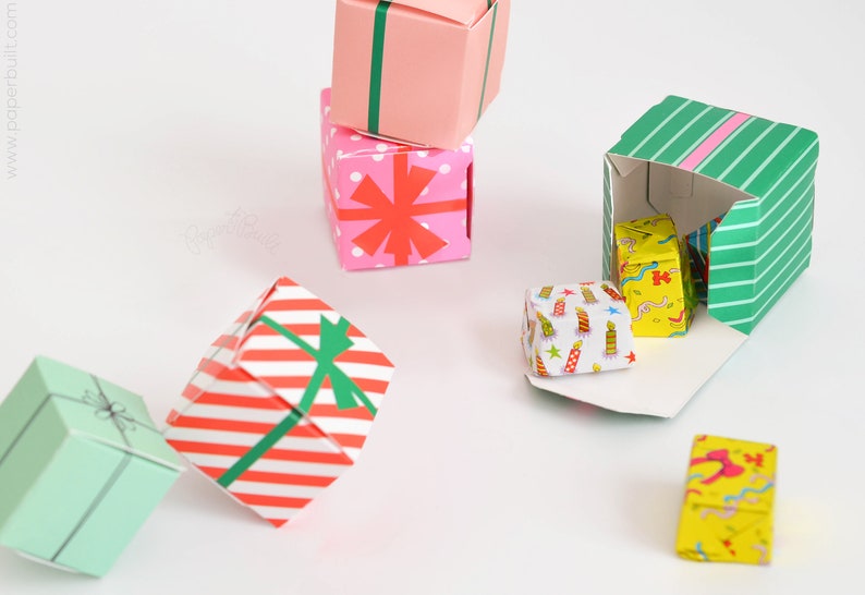 May include: A collection of colorful origami gift boxes with various patterns, including red and white stripes, pink with red stars, green with white stripes, and yellow with a birthday cake design. Some boxes are open, revealing smaller boxes inside.