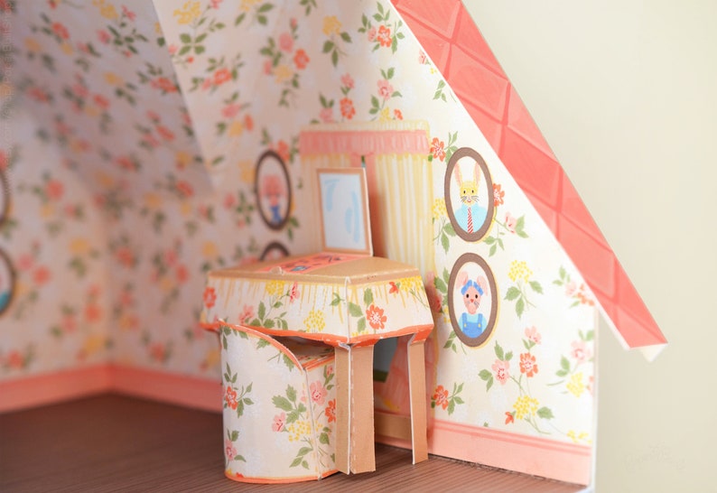 May include: A miniature dollhouse room with floral wallpaper, a small table with a floral tablecloth, and a chair with floral upholstery. There are three framed pictures on the wall with illustrations of rabbits and a mouse.