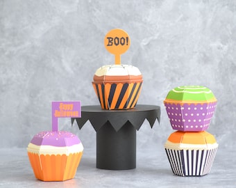 May include: Three Halloween-themed paper cupcakes with orange, purple, and green frosting. The cupcakes are decorated with stripes, polka dots, and a swirl design. The cupcakes are topped with flags that say "Boo!" and "Happy Halloween".