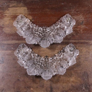 Könnte beinhalten: Zwei klare, dekorative Glasstücke mit floralem Design. Jedes Stück ist gebogen und weist detaillierte Blatt- und Blumenmuster auf. Das Glas hat ein mattiertes Aussehen, und die Stücke werden auf einer Holzoberfläche präsentiert.