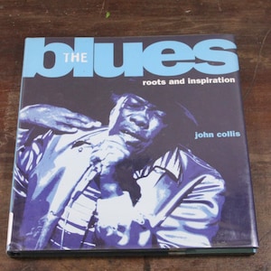 May include: A book titled "The Blues: Roots and Inspiration" by John Collis. The cover features a black and white photo of a man singing into a microphone.