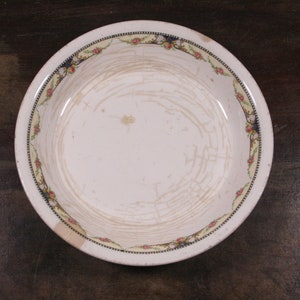 May include: A white ceramic bowl with a floral design around the rim. The bowl has a worn, vintage look with visible scratches and crazing.