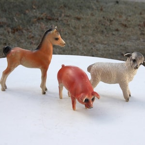 Könnte beinhalten: Drei Plastik-Bauernhoftierfiguren: ein braunes Pferd, ein rosa Schwein und ein weißes Schaf.