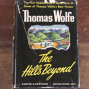 May include: A black hardback book with a yellow title, "The Hills Beyond" by Thomas Wolfe. The book cover features a painting of a river winding through a valley with mountains in the background.