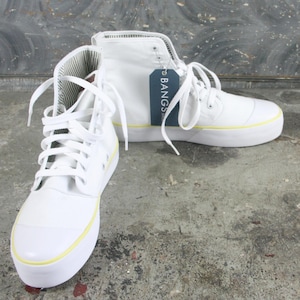 May include: Pair of white high-top sneakers with white laces and a yellow stripe along the sole. The sneakers have a canvas upper and a tag that reads "BANGS". The interior lining has a striped pattern.