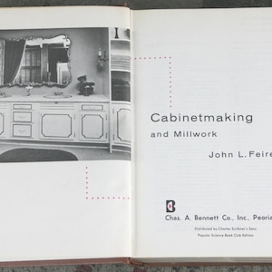 Può includere: Un libro con copertina rigida aperto intitolato Cabinetmaking and Millwork di John L. Feirer. La pagina sinistra presenta una fotografia in bianco e nero di un mobile da bagno con specchio. La pagina destra mostra titolo, autore ed editore.