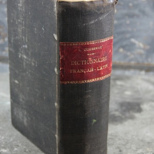 May include: A black, worn, hardback book with a red and gold label that reads "Dictionnaire Français - Latin" by L. Quicherat.