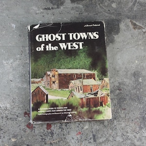 May include: A vintage book titled "Ghost Towns of the West" with a sunset pictorial cover featuring a photograph of an abandoned town in the western United States. The book is a pictorial guide to towns and mining camps that opened the West.