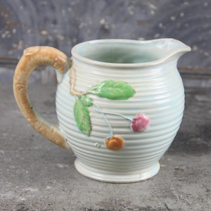 Puede incluir: Jarra de cerámica azul claro con diseño acanalado. La jarra tiene un asa marrón y está decorada con hojas verdes y cerezas rosas y naranjas. Tiene un pico para verter fácilmente.