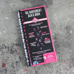 Może przedstawiać: Czarna książka z różowym grzbietem zatytułowana "The Bartender's Black Book 7th Edition". Książka zawiera kolekcję przepisów na napoje na XXI wiek, z ponad 2700 przepisami, w tym 100 nowymi przepisami. Zawiera również sekcję o aromatyzowanych wódkach, ginach i rumie, a także napoje deserowe, shoty i floaty.