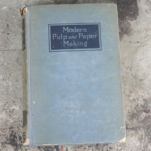 以下が含まれることがあります： 「Modern Pulp and Paper Making」というタイトルが暗い青色の長方形で示された、薄い青色の表紙の古い本。本の表紙には、摩耗や経年劣化の兆候が見られます。
