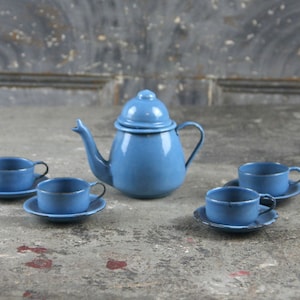 Könnte beinhalten: Ein blaues Emaille-Tee-Set mit einer Teekanne und vier Tassen und Untertassen. Das Set ist aus Metall und hat einen Vintage-Look.