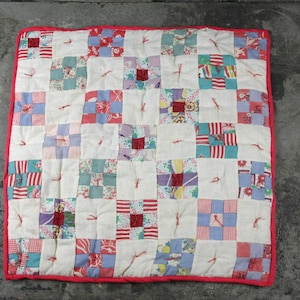 May include: A patchwork quilt with a white background and squares of various colors and patterns, including red, blue, green, and pink. The quilt is edged with a red border.