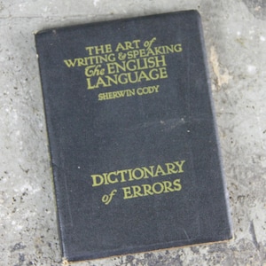 May include: A vintage book with a dark cover and gold lettering. The title reads "THE ART of WRITING & SPEAKING The ENGLISH LANGUAGE" by Sherwin Cody. The book also features the title "DICTIONARY of ERRORS".