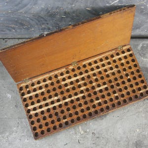 May include: An open, vintage wooden box with a hinged lid. The box is rectangular with numerous circular holes arranged in a grid pattern. The wood has a warm, natural tone with visible grain and some wear.