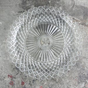 May include: Clear glass serving plate with a diamond pattern around the rim and a radial design in the center. The plate is circular and appears to be vintage or antique, suitable for serving appetizers or desserts.