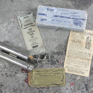 Peut inclure: Ensemble d'outils et d'emballages vintage, dont un micromètre, une boîte intitulée "Certified Accuracy Micrometer" et des documents imprimés de The Central Tool Co. et Lenk Mfg. Company. Les outils sont de couleur argentée.