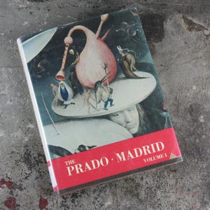 May include: The cover of a book titled "The Prado, Madrid, Volume I". The cover features a painting of a surreal scene with a large, pink, bulbous object in the center. The painting is in a style reminiscent of Hieronymus Bosch.