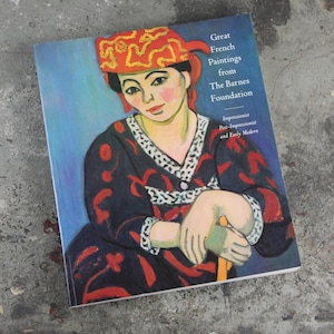 May include: Book cover featuring a painting of a woman wearing a red and gold patterned headscarf. The title of the book is "Great French Paintings from The Barnes Foundation." The subtitle is "Impressionist, Post-Impressionist and Early Modern."