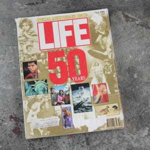 May include: A vintage LIFE magazine cover, a special anniversary issue. The cover features a collage of images, including portraits and historical moments. The magazine's title is in red, with the number "50" prominently displayed.