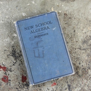 Può includere: Un libro rilegato in blu intitolato "New School Algebra" di Wentworth.