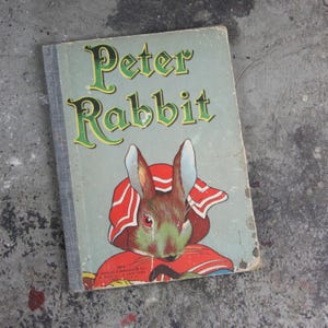 May include: Vintage children's book titled "Peter Rabbit." The cover features a green and brown rabbit wearing a red bonnet. The title is in green and yellow lettering. The book has a light blue cover with visible wear and tear.