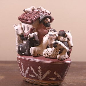 Könnte beinhalten: Eine Keramikfigur von Noahs Arche mit einem braunen Dach, einem weißen Haus und einem bärtigen Mann, der auf dem Dach steht. Die Arche ist gefüllt mit Tieren, darunter eine braune und weiße Kuh, ein weißes Schaf und eine weiße Ziege.
