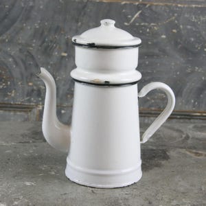 Puede incluir: Cafetera de esmalte blanco con borde negro y tapa. La cafetera tiene un pico y una manija.