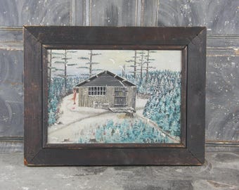 May include: A framed painting depicts a cabin in a snowy forest scene. The cabin is gray with a dark roof, and a figure in red stands on a path. The artwork is signed "H.A. LARRE" in the lower right corner.