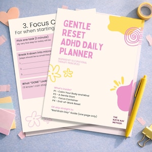 May include: A Gentle Reset ADHD Daily Planner with a pink and yellow design, and a worksheet. The planner includes sections for focus, and breaking down tasks. A yellow pen and tape are also visible.