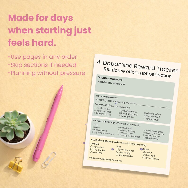 May include: A pink pen, a succulent plant in a white pot, a gold binder clip, and a paperclip are arranged on a light yellow surface. A printed sheet titled "Dopamine Reward Tracker" is also present, with text about self-validation and rewards.