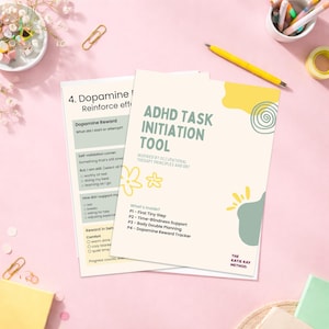 May include: Two printed worksheets on a pink surface. The top sheet is titled "ADHD Task Initiation Tool" with a floral design. The second sheet is titled "4. Dopamine/Reinforce eff". Stationery items, including pens and paperclips, are scattered around.