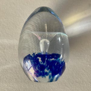 May include: A clear glass paperweight in the shape of an egg with a blue and white swirl inside.