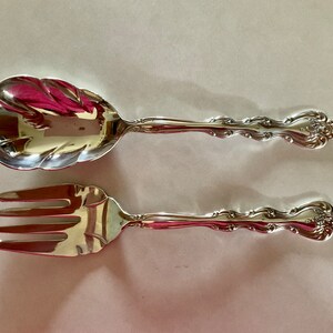 May include: A silver serving set with a fork and spoon. The handles are ornate and have a floral design.