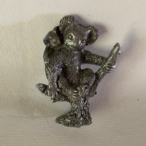 May include: A silver-toned metal figurine of a koala holding a joey, perched on a tree branch.