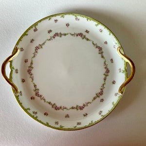 May include: A white porcelain serving platter with gold handles and a green and pink floral design.