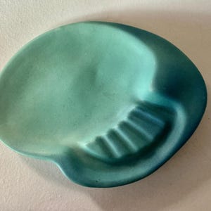 May include: A skull-shaped ceramic tray featuring a smooth matte finish with a gradient color scheme that transitions from a light mint green on the left side to a deep, saturated teal blue on the right side, including molded teeth details.