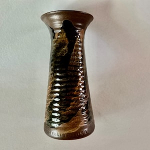 May include: A handcrafted, brown ceramic vase with a textured, ridged design. The vase has a flared top and a dark brown, glossy finish. The base of the vase has the text "Grey USA".