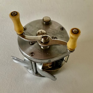 May include: A silver South Bend No. 350 Level Winding Antibacklash fishing reel with two wooden knobs. The reel has a gold-colored line on the spool.
