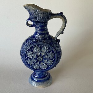 May include: A blue and white ceramic pitcher with a floral design. The pitcher has a round body and a handle. It is a traditional German style.