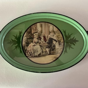 May include: Oval serving tray with a light green border and a central image of people in period clothing. The tray has black handles and a decorative leaf design on the green surface. The tray is likely vintage.