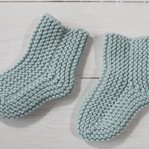 May include: A pair of light blue knitted socks. The socks are made with a simple stitch pattern and have a soft, cozy look.