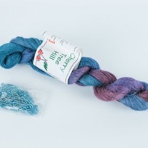 May include: A skein of teal and purple yarn with a label that reads "Cherry Tree Hill" and a small bag of teal beads.